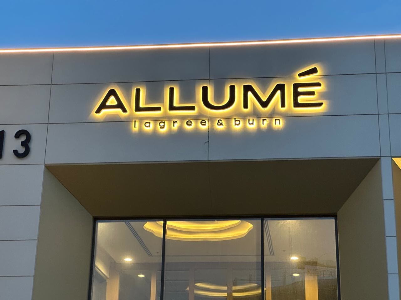 Illuminated Allumé signage over the studio entrance at dusk